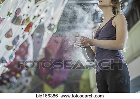 Stock Photograph - Athlete chalking her hands at rock wall in gym. Fotosearch