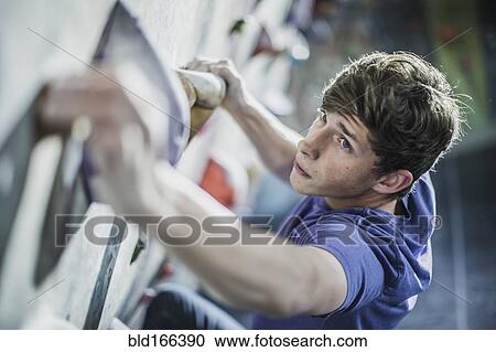 Stock Image - Athlete climbing rock wall in gym. Fotosearch