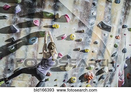 Stock Image - Athlete climbing rock wall in gym. Fotosearch