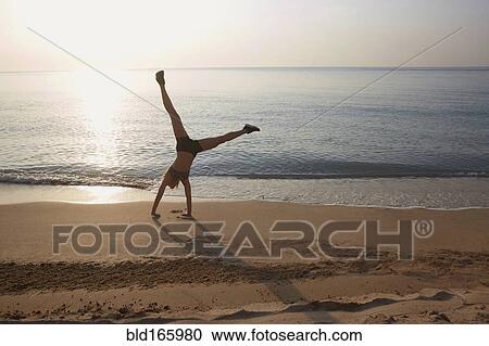 Stock Image - Athlete doing cartwheel on beach. Fotosearch