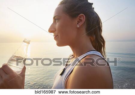 Stock Photo - Athlete drinking water bottle on beach. Fotosearch