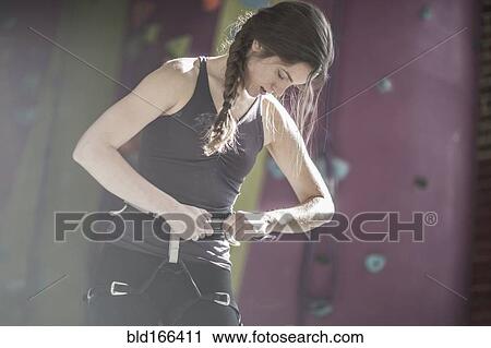 Stock Image - Athlete fastening climbing harness in gym. Fotosearch