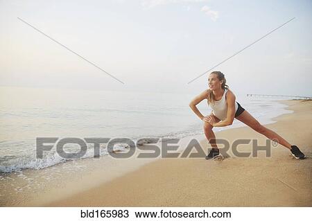 Stock Image - Athlete stretching on beach. Fotosearch