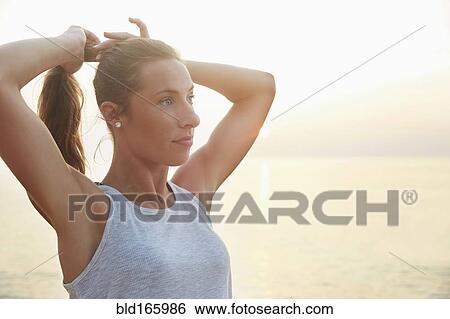 Stock Photograph - Athlete tying hair in ponytail on beach. Fotosearch