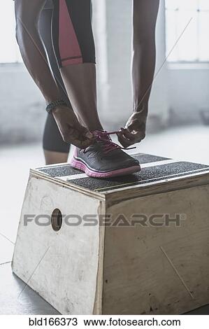 Stock Image - Athlete tying her shoes on platform in gym. Fotosearch