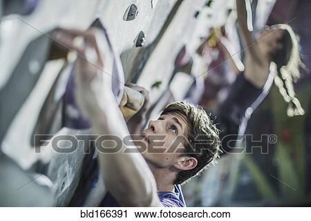 Stock Image - Athletes climbing rock wall in gym. Fotosearch