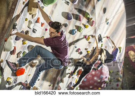 Stock Image - Athletes climbing rock wall in gym. Fotosearch