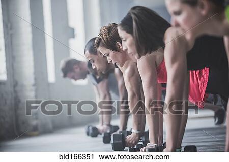 Stock Image - Athletes doing push-ups and lifting weights on floor. Fotosearch