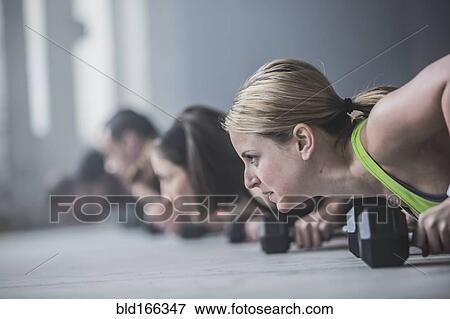 Stock Photo - Athletes doing push-ups and lifting weights on floor. Fotosearch