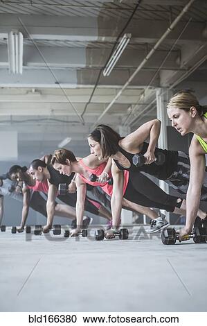 Stock Image - Athletes doing push-ups with dumbbells on floor. Fotosearch