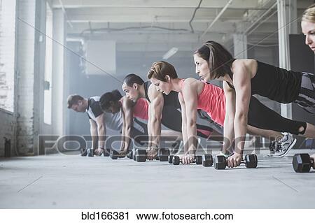 Stock Image - Athletes doing push-ups with dumbbells on floor. Fotosearch