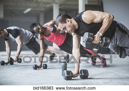 Stock Image - Athletes doing push-ups with dumbbells on floor. Fotosearch