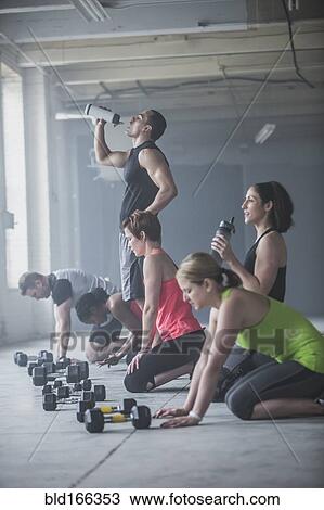 Stock Image - Athletes drinking water bottles near dumbbells. Fotosearch