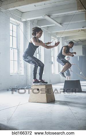 Stock Image - Athletes jumping on platforms in gym. Fotosearch