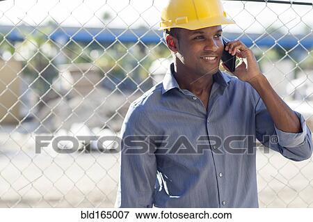 Stock Photo - Black architect in hard hat talking on cell phone. Fotosearch