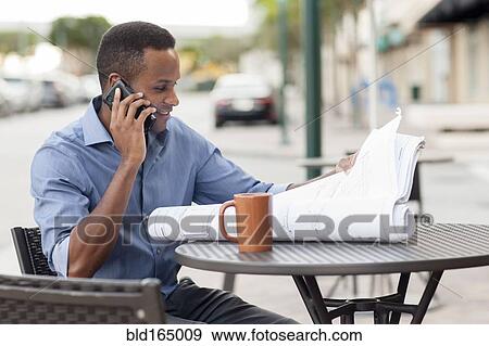 Stock Photo - Black architect talking on cell phone and reading blueprints. Fotosearch