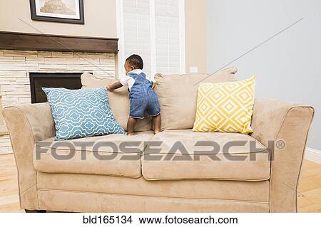 Black baby climbing on sofa in living room View Large Photo Image Picture - Black baby climbing on sofa in living room. Fotosearch
