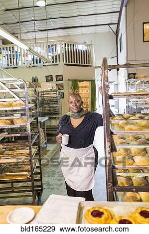 Stock Photo - Black baker drinking coffee in bakery kitchen. Fotosearch