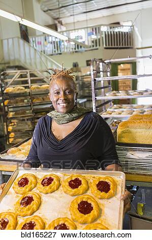 Stock Photo - Black baker holding tray of pastries in bakery kitchen. Fotosearch