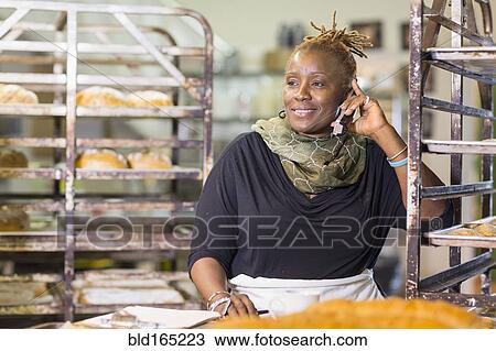 Black baker talking on cell phone in bakery kitchen View Large Photo Image Stock Image - Black baker talking on cell phone in bakery kitchen. Fotosearch