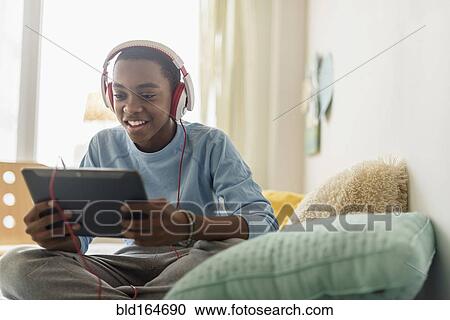 Stock Image - Black boy in headphones using digital tablet. Fotosearch