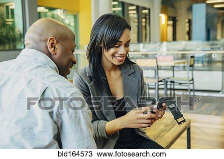 Stock Image - Black business people using cell phone in cafe. Fotosearch
