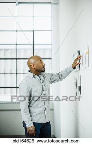 Stock Photograph - Black businessman examining paperwork on office wall. Fotosearch