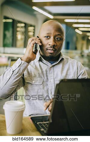 Stock Photo - Black businessman talking on cell phone in cafe. Fotosearch