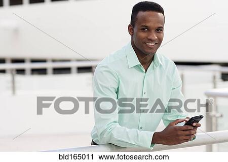 Stock Image - Black businessman using cell phone on balcony. Fotosearch