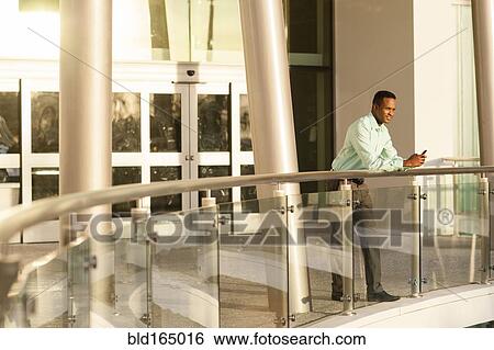 Black businessman using cell phone on railing View Large Photo Image Stock Photograph - Black businessman using cell phone on railing. Fotosearch