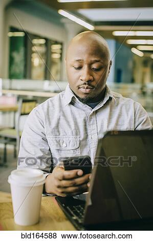 Stock Photo - Black businessman using laptop and cell phone in cafe. Fotosearch
