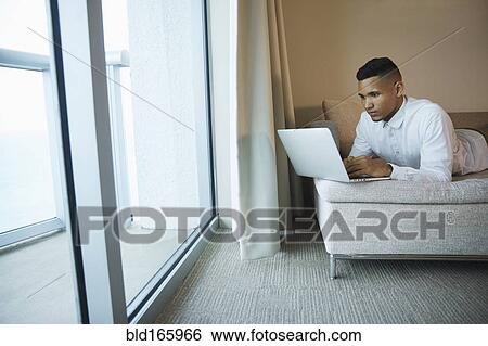 Stock Photograph - Black businessman using laptop in hotel room. Fotosearch
