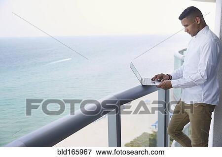 Stock Photo - Black businessman using laptop on balcony. Fotosearch