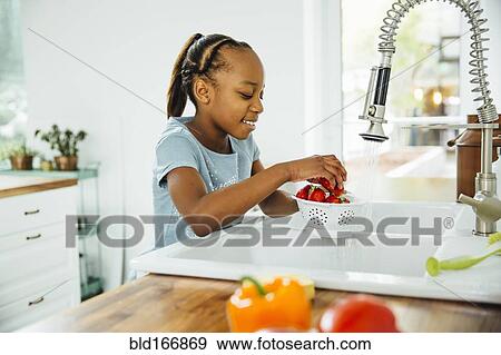 Stock Photo - Black girl washing strawberries in kitchen. Fotosearch