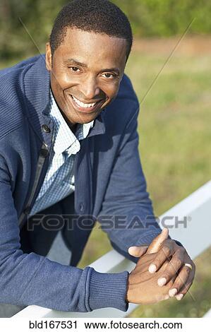 Stock Image - Black man leaning on fence outdoors. Fotosearch