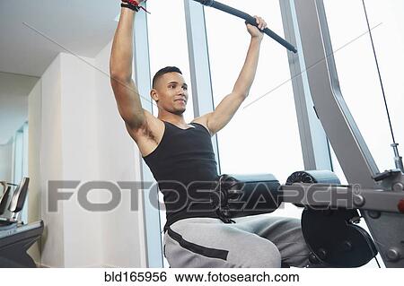 Stock Photograph - Black man using exercise machine in gym. Fotosearch