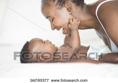 Stock Photo - Black mother and baby playing on bed. Fotosearch