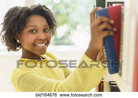 Stock Photograph - Black student choosing book from library shelf. Fotosearch