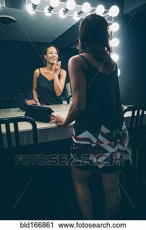 Stock Image - Black woman applying makeup in vanity mirror. Fotosearch