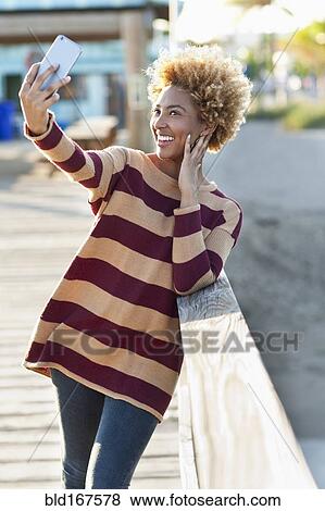 Stock Photo - Black woman taking selfie on wooden boardwalk. Fotosearch