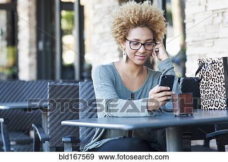 Stock Photo - Black woman using cell phone at cafe. Fotosearch