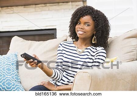 Stock Photograph - Black woman watching television on sofa. Fotosearch