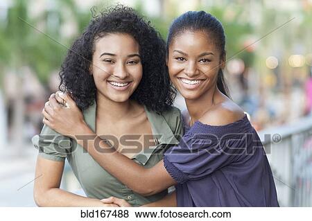 Stock Photo - Black women hugging on balcony. Fotosearch