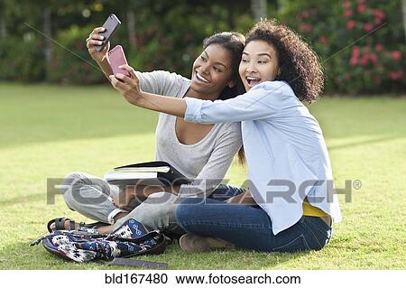 Stock Image - Black women taking selfies in park. Fotosearch