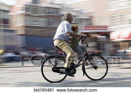 Stock Image - Blurred view of father and son bicycling on city street. Fotosearch