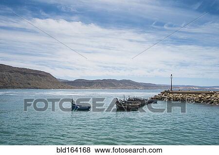 Boats docked on rocky pier in remote harbor View Large Photo Image Stock Photo - Boats docked on rocky pier in remote harbor. Fotosearch