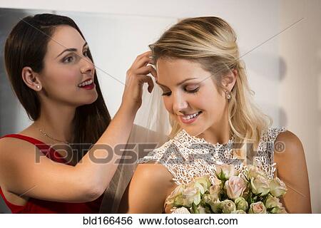 Stock Photograph - Bridesmaid adjusting veil of bride before wedding. Fotosearch
