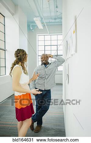 Stock Image - Business people discussing paperwork on office wall. Fotosearch