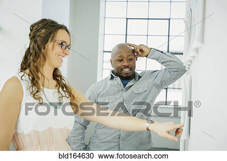 Business people examining paperwork on office wall View Large Photo Image Stock Image - Business people examining paperwork on office wall. Fotosearch