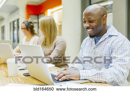 Stock Image - Business people working on laptops in office meeting. Fotosearch